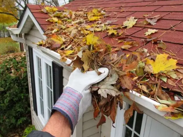 gloved hand cleaning leaves out of gutters